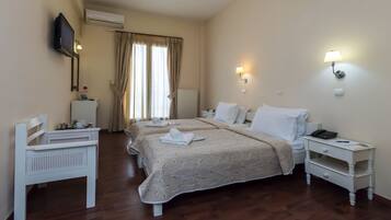 A hotel room with two beds, a desk, a chair, a TV, and a nightstand with a lamp.