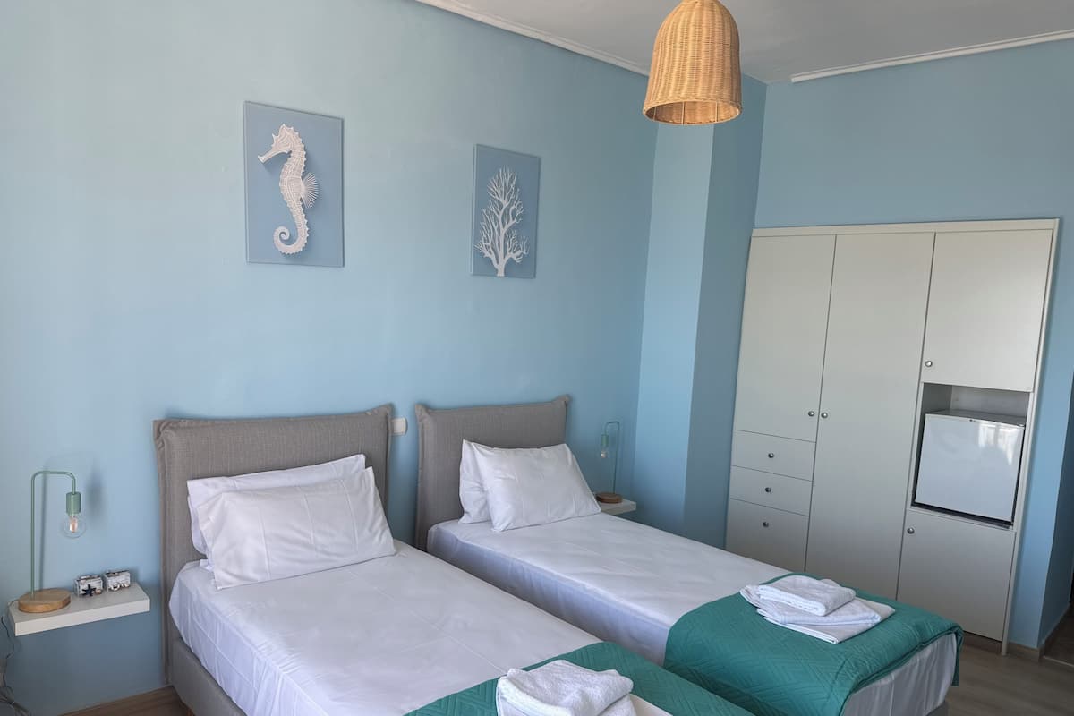 A hotel room with two beds, a wardrobe, a hanging light fixture, and wall art.