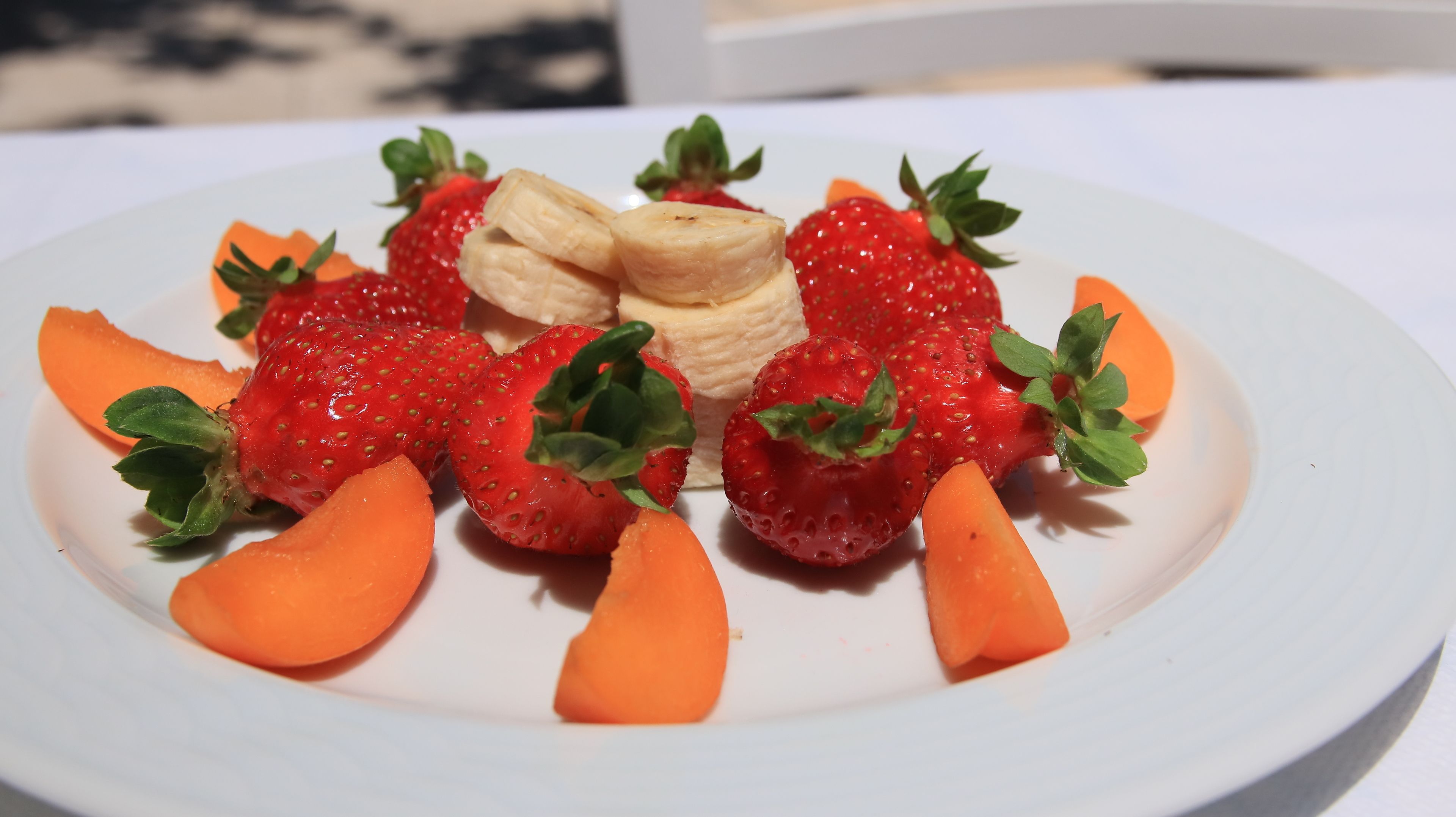 A plate of sliced strawberries, banana slices, and carrot sticks.