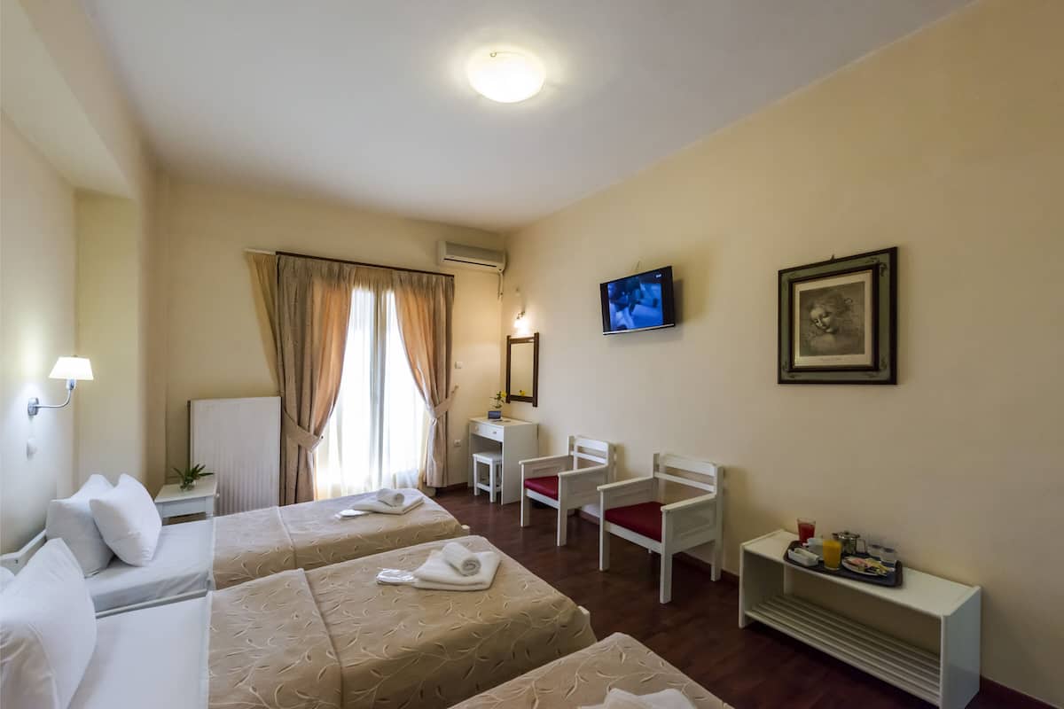 A hotel room with two beds, a desk, a chair, a TV, and a small table with a tray of breakfast items.