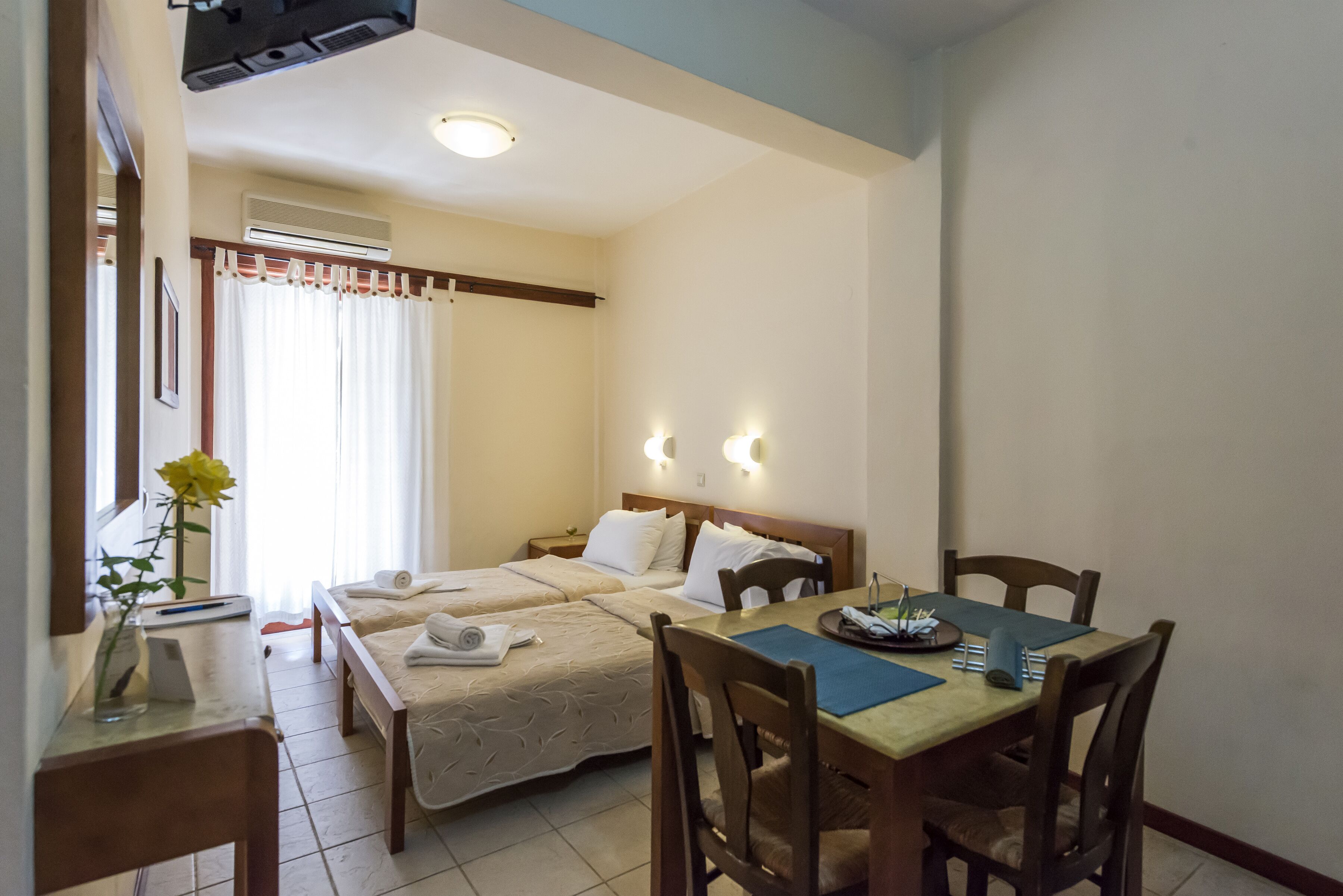 A hotel room with two beds, a dining table, and a small kitchen area.
