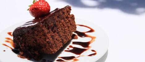 Uma fatia de bolo de chocolate com uma morango por cima, servida em um prato branco com calda de chocolate.