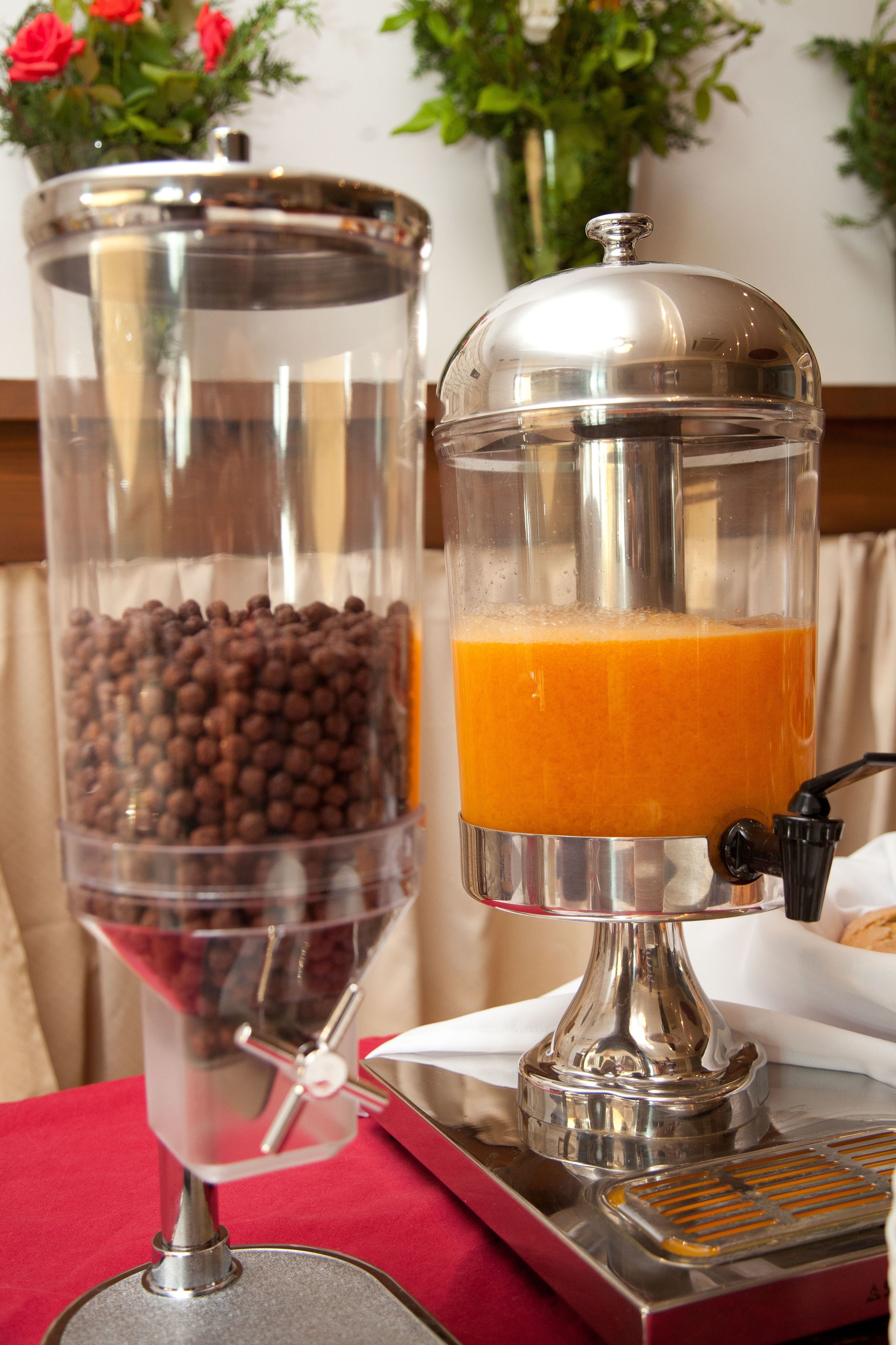 A coffee machine with a transparent container filled with coffee beans and a glass container with orange juice.