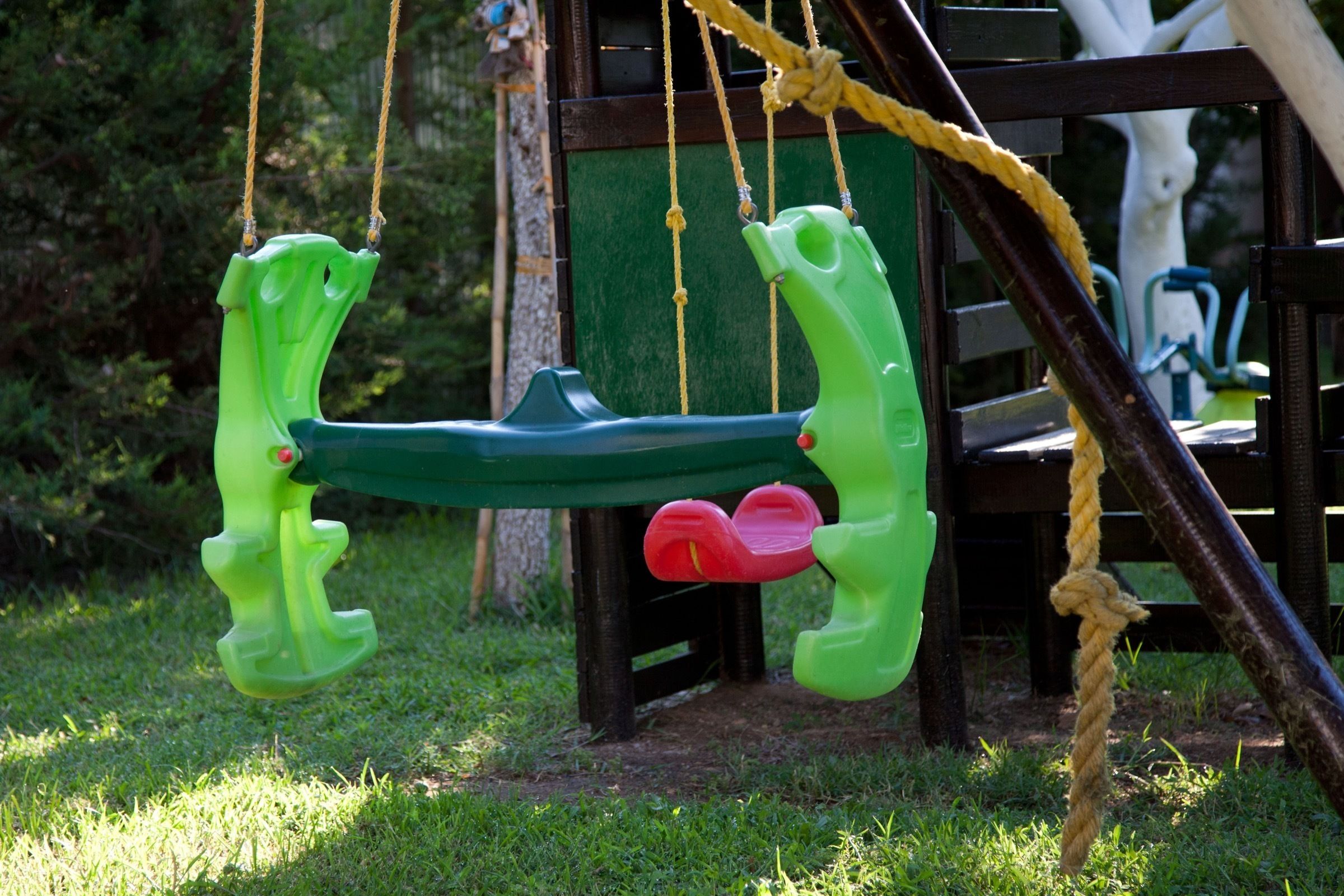 A green swing set with two seats and a rope.