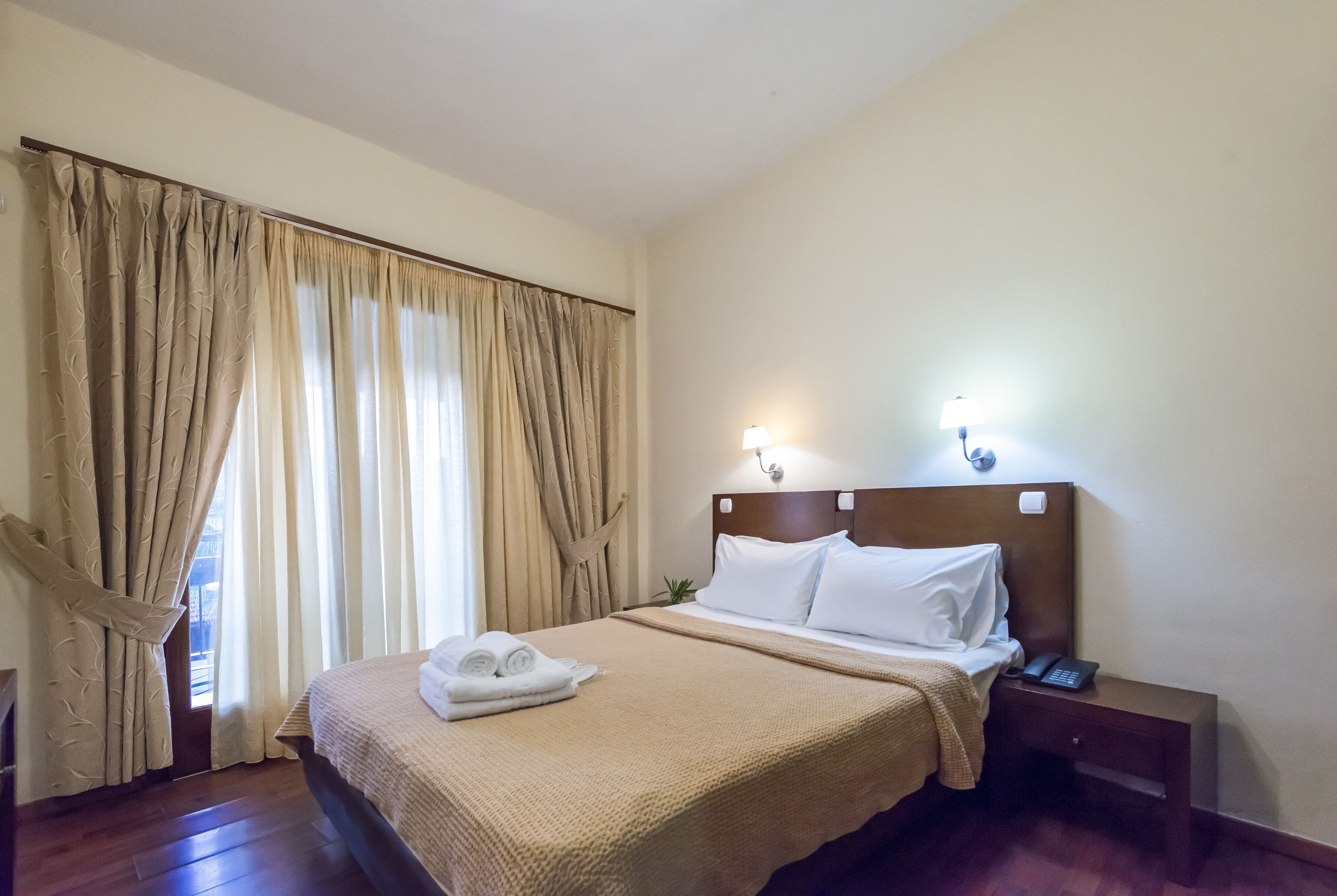 Habitación de hotel con cama, mesita de noche con teléfono, lámpara y cortinas.