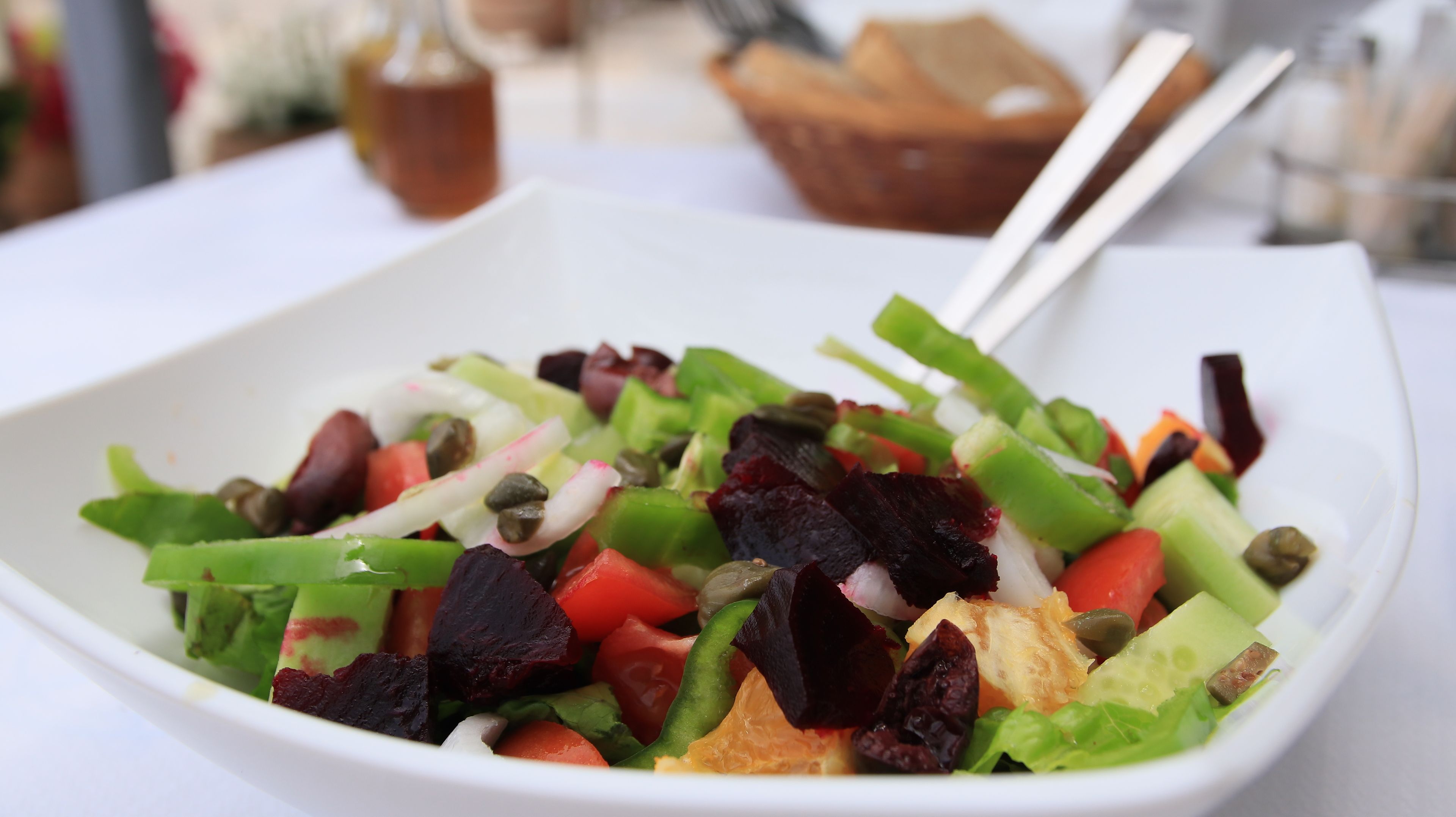 A white bowl containing a salad with various vegetables and a piece of bread.