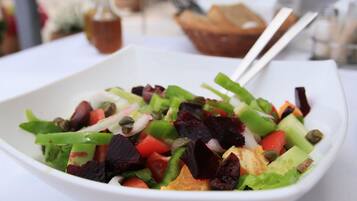 A white bowl containing a salad with various vegetables and a piece of bread.