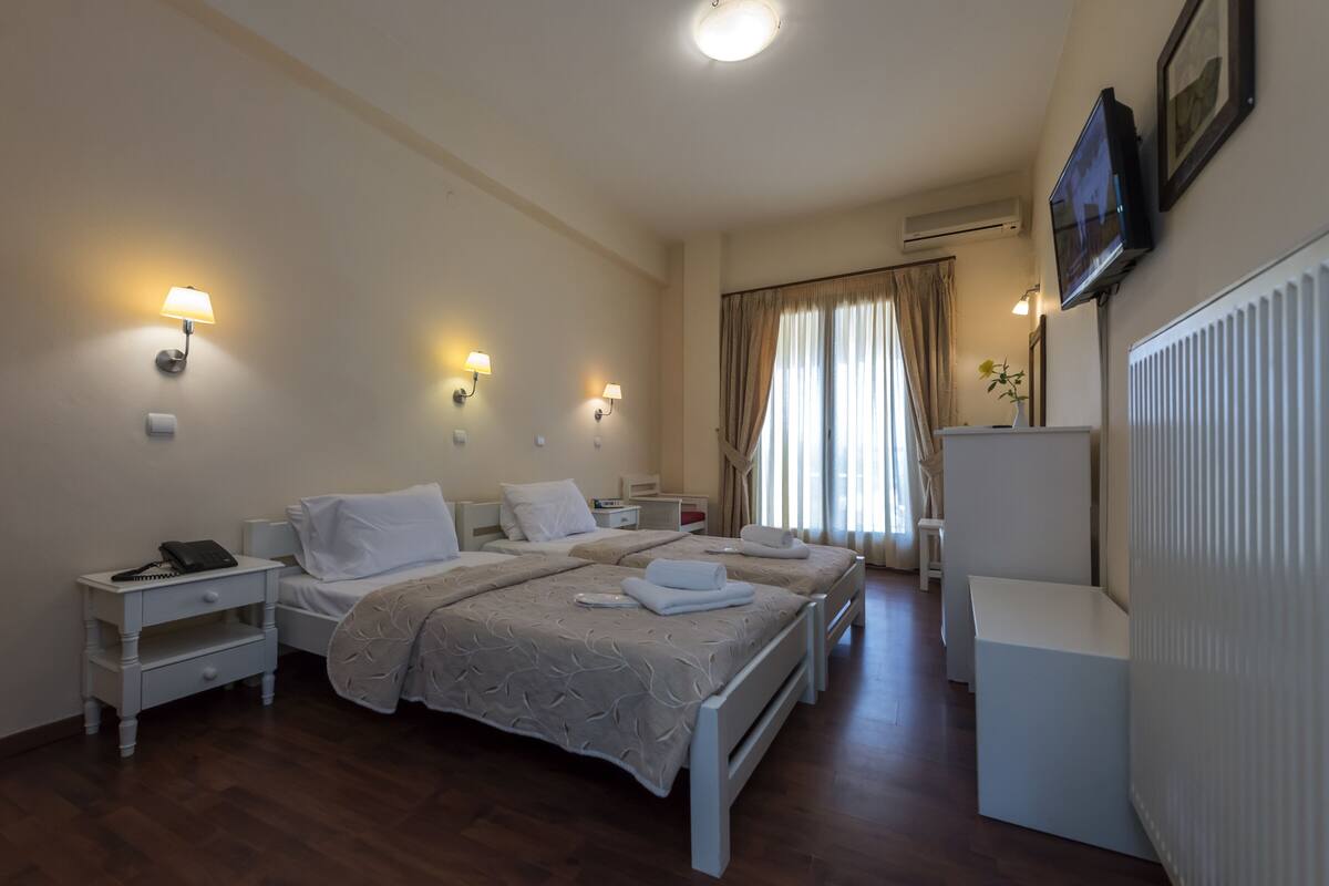 A hotel room with two beds, bedside tables, a desk, a chair, a TV, and a window with curtains.