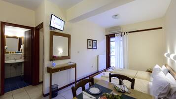 Habitación de hotel con comedor, televisor montado en la pared, sofá y baño con lavamanos y espejo.