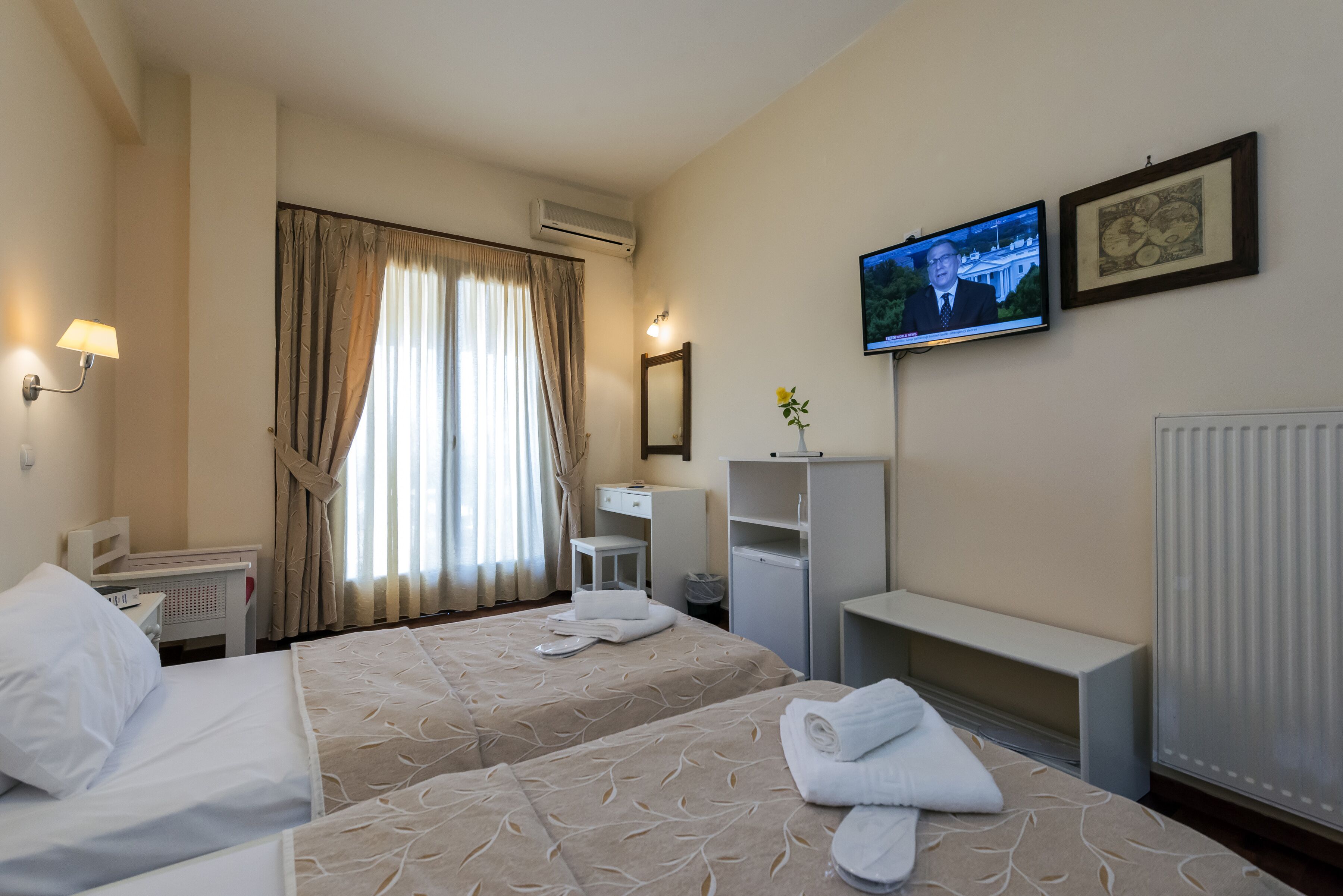 Una camera d'albergo con due letti, televisore, scrivania, sedia e termosifone.