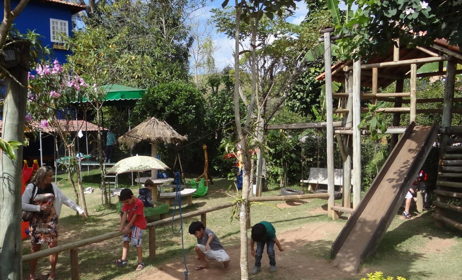 A playground with slides, climbing structures, and a thatched-roof shelter.