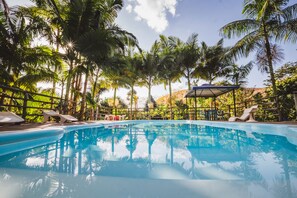 A clear blue swimming pool surrounded by palm trees and a wooden deck with lounge chairs. - Hotel Pousada Vovozinho (Guacui)