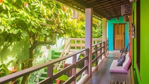A covered outdoor area with a wooden railing, a bench, and a door leading to a building.