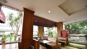 Un restaurant avec des banquettes en bois, un présentoir de desserts et une vue sur les palmiers à l’extérieur.