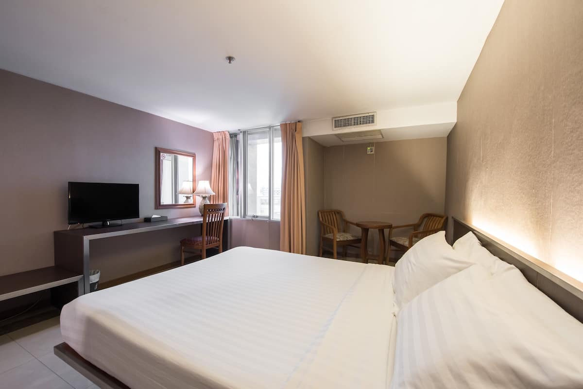 Quarto de hotel com cama, escrivaninha com televisão, duas cadeiras e janela com cortinas.