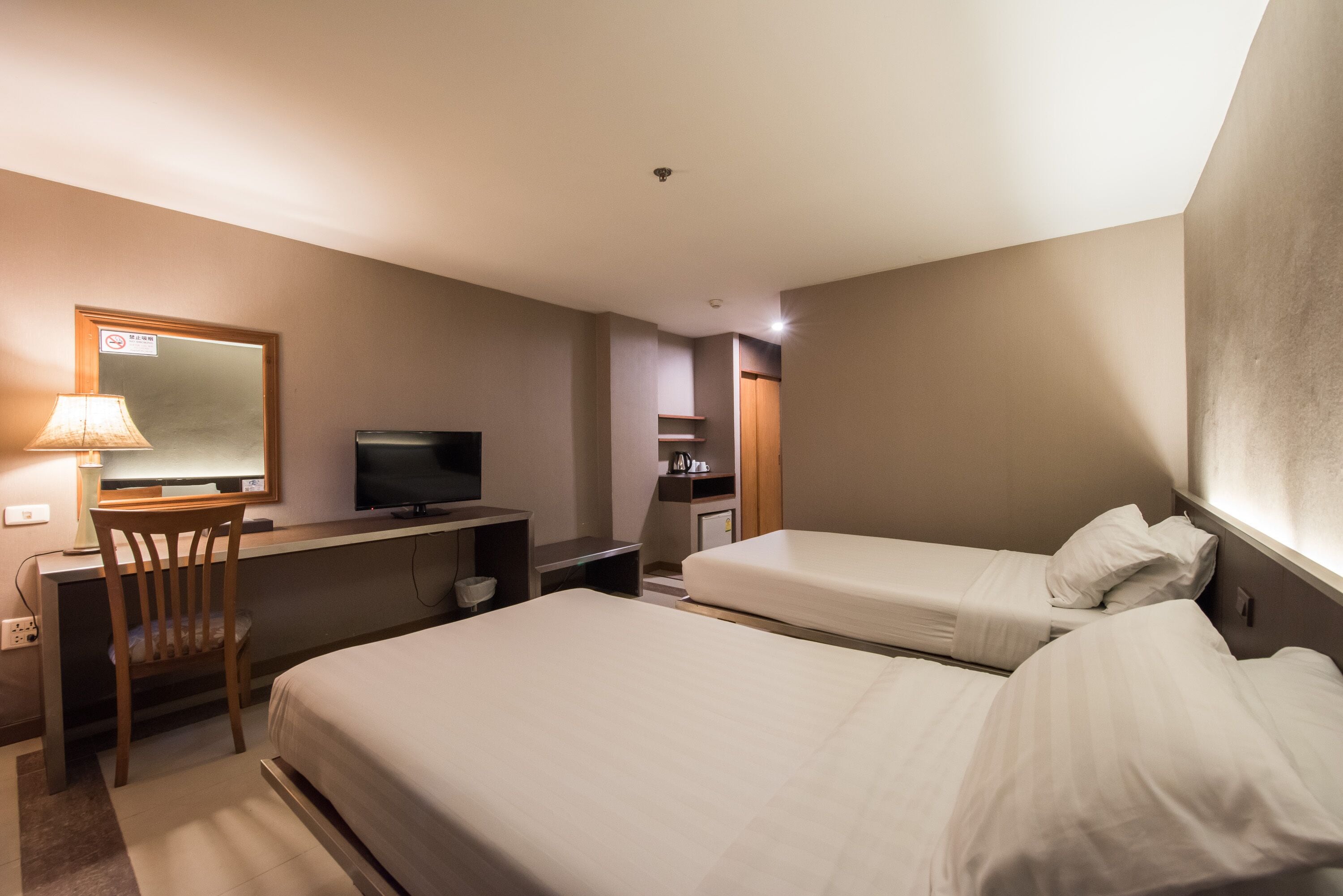 A hotel room with two beds, a desk with a chair, a television, and a small kitchenette.