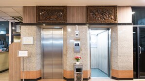 Un hall d’entrée doté de deux ascenseurs, d’un comptoir de réception et d’une petite table sur laquelle est posé un vase de fleurs.