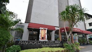 La façade de l’hôtel Bangkok City Suite, avec une grande banderole, des auvents rouges et des plantes en pot.
