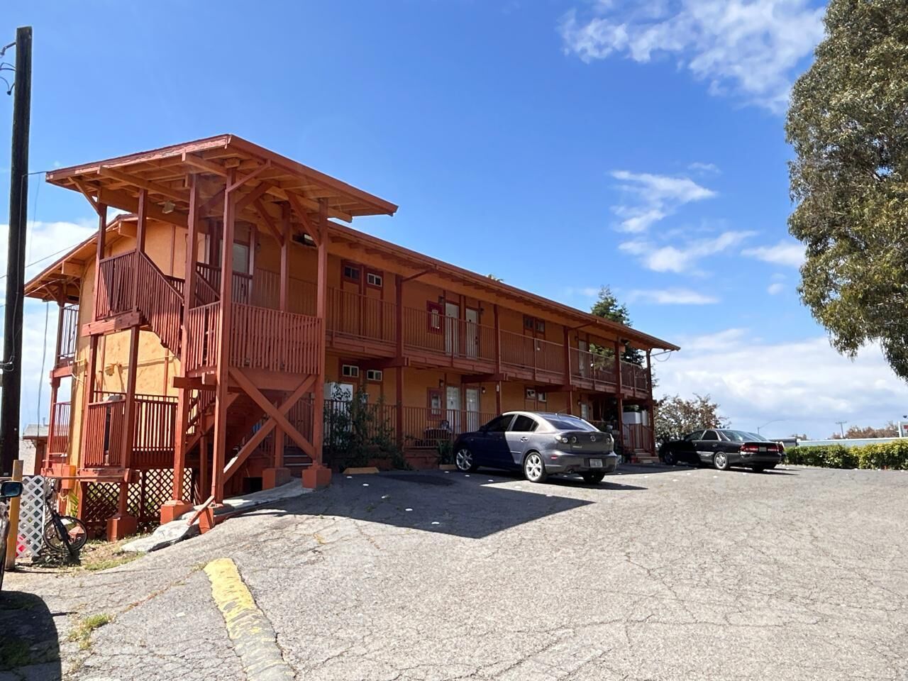 A two-story building with a balcony, a covered porch, and a parking area with two cars.