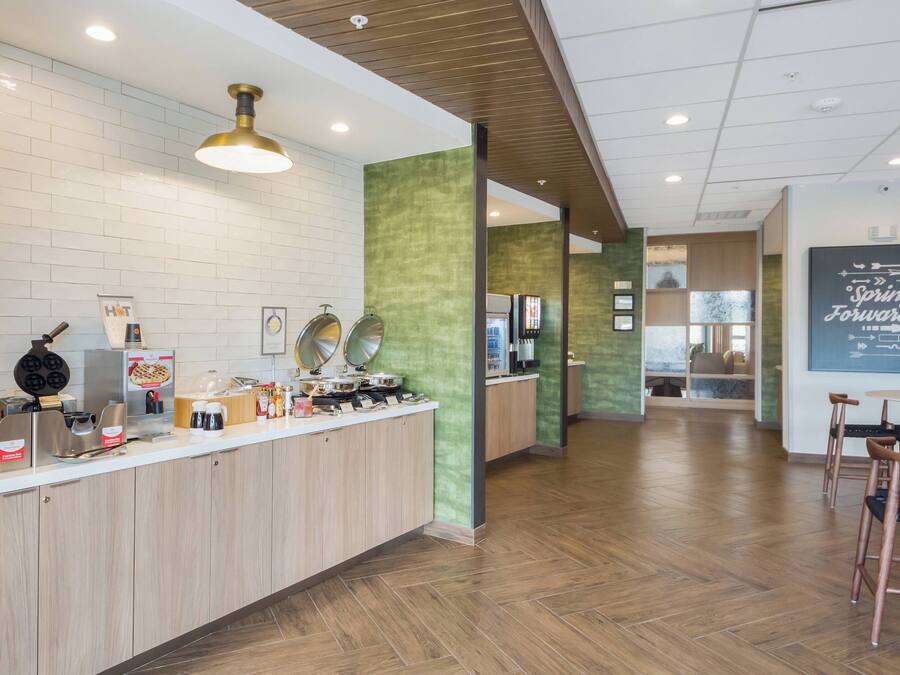 A modern kitchen area with a counter, waffle maker, coffee station, and a view into a dining area.