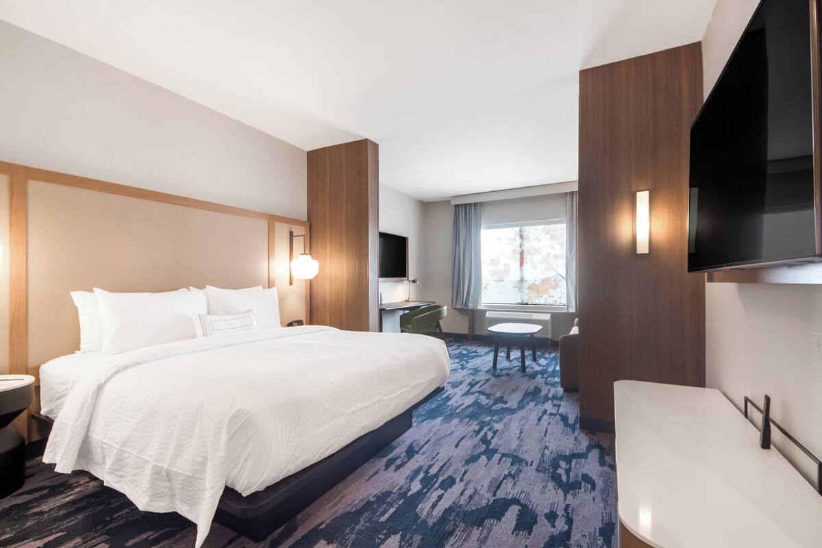 A hotel room with a large bed, a desk, a chair, a TV, and a window with curtains.