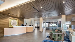 A spacious lobby with a reception desk, a dining area, and a seating area with a blue patterned rug. - Fairfield Inn & Suites by Marriott Dallas Plano/Frisco (Plano)