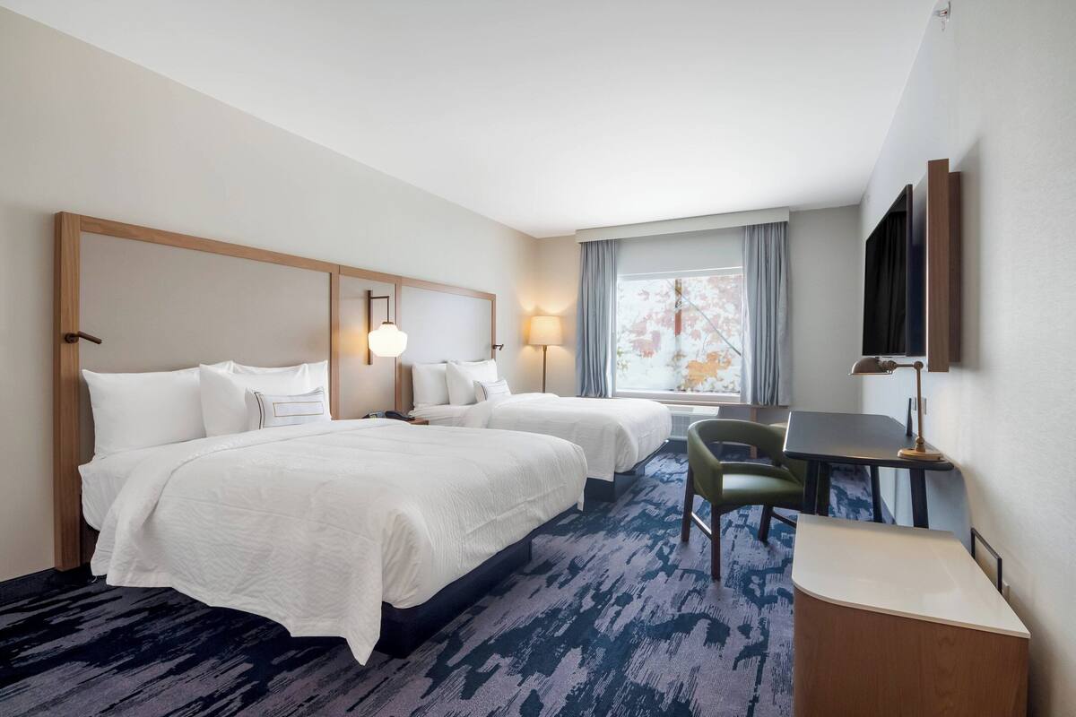 A hotel room with two beds, a desk, a chair, a TV, and a window with curtains.