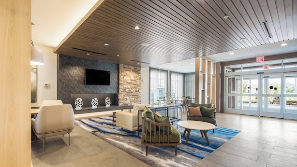 A spacious lobby with a modern design, featuring a stone wall, a flat-screen TV, comfortable seating, and a large glass door leading outside. - Fairfield Inn & Suites by Marriott Dallas Plano/Frisco (Plano)