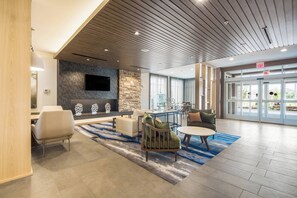 A spacious lobby with a modern design, featuring a stone wall, a flat-screen TV, comfortable seating, and a large glass door leading outside. - Fairfield Inn & Suites by Marriott Dallas Plano/Frisco (Plano)