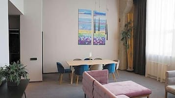 Ein modernes Wohnzimmer mit Esstisch, Stühlen, einem rosafarbenen Sofa und zwei Bildern an der Wand.