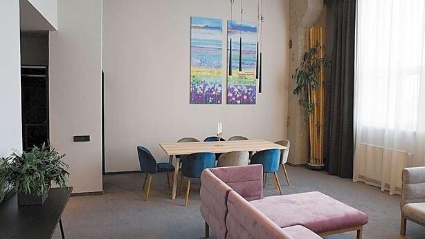 A modern living room with a dining table, chairs, a pink sofa, and two paintings on the wall.