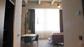 Ein Zimmer mit Esstisch, Stühlen, einer Couch und einem großen Fenster mit Vorhängen.