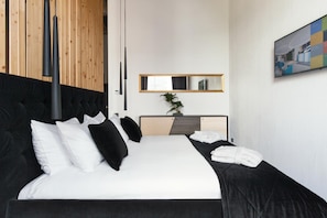 Un hotel moderno con una cama grande, un cabecero de madera, una mesita de noche con una planta, un espejo y un cuadro en la pared.