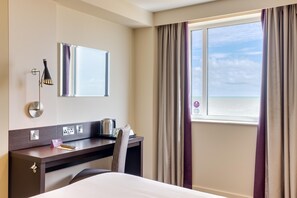 Ein Hotelzimmer mit einem Bett, einem Schreibtisch mit Wasserkocher, einem Spiegel und einem Fenster mit Vorhängen.