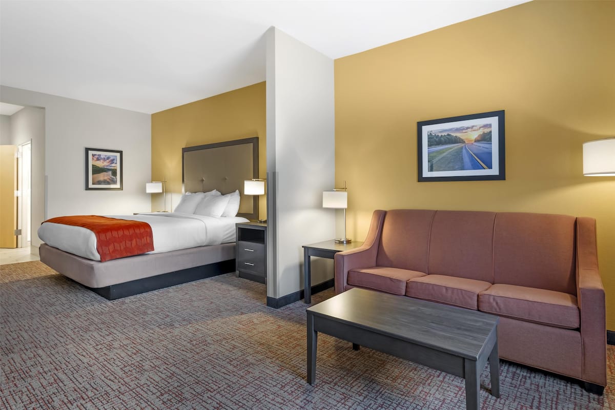 A hotel room with a bed, a sofa, a coffee table, and two bedside tables.