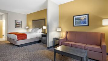 Quarto de hotel com cama, sofá, mesa de centro e duas mesas de cabeceira.