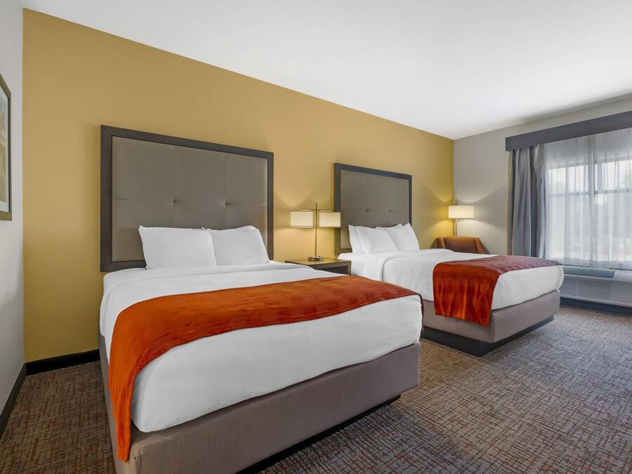 A hotel room with two beds, a large window with curtains, and a carpeted floor.
