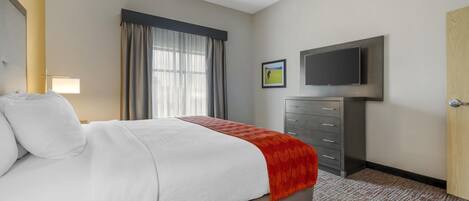 A hotel room with a bed, a television mounted on the wall, a dresser, and a window with curtains.