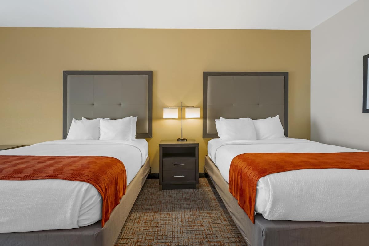 A hotel room with two beds, a nightstand between them, and a lamp.