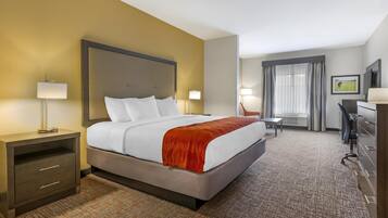 A hotel room with a large bed, a desk, a chair, a TV, and a window with curtains.