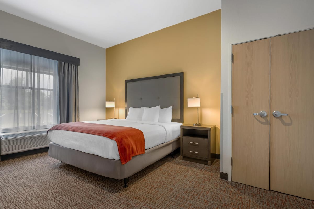 A hotel room with a bed, bedside lamps, a wardrobe, and a window with curtains.