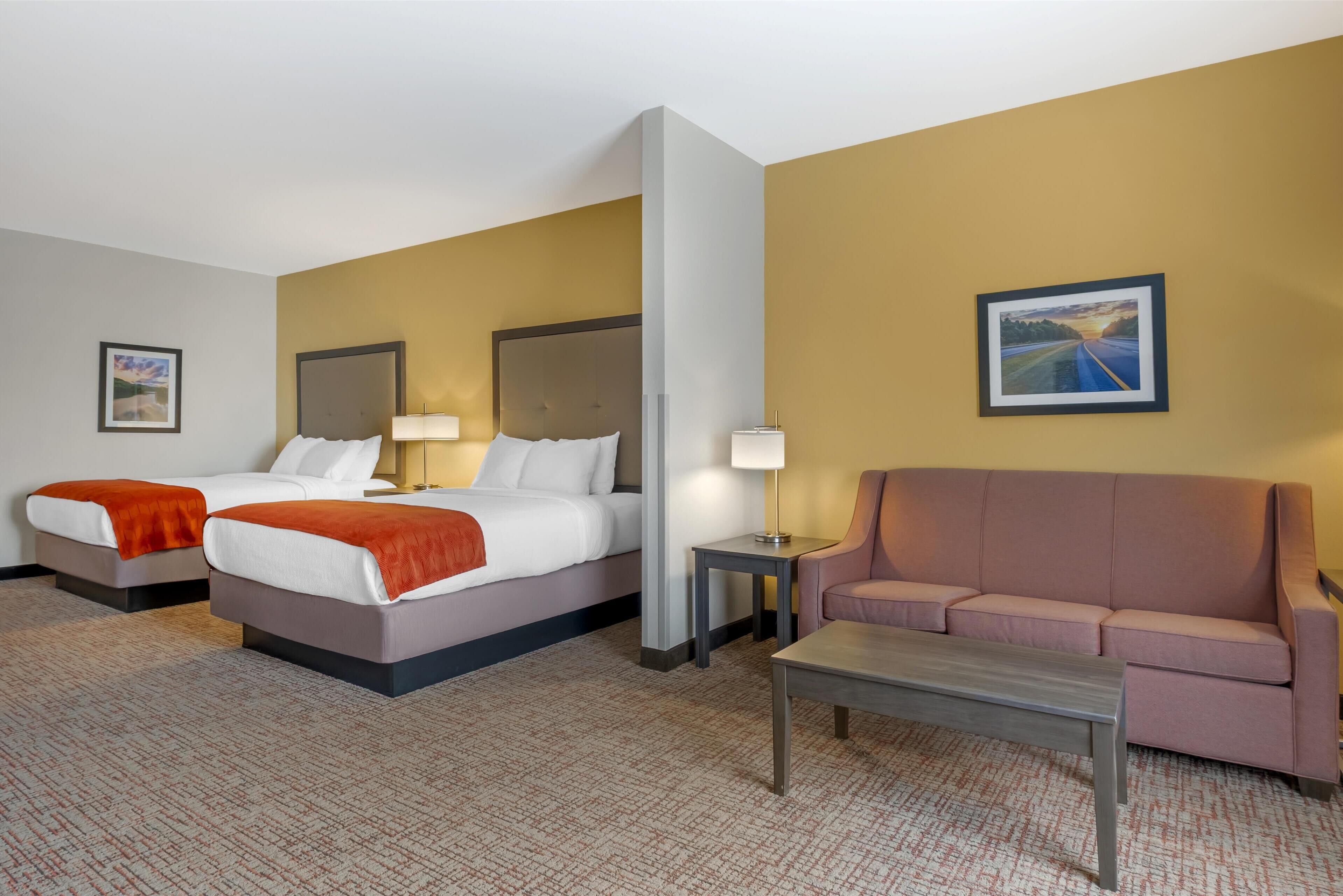 A hotel room with two beds, a sofa, a coffee table, and a painting on the wall.