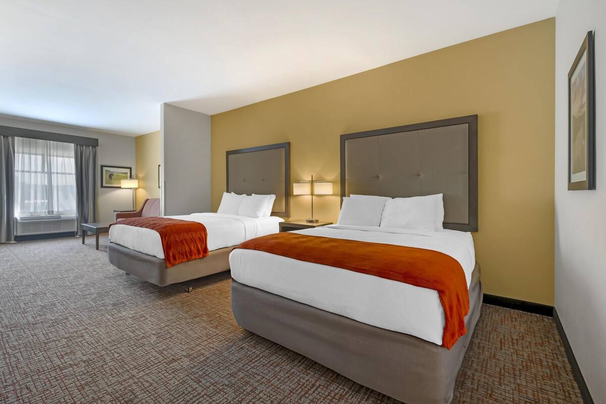 A hotel room with two beds, a desk, and a chair.