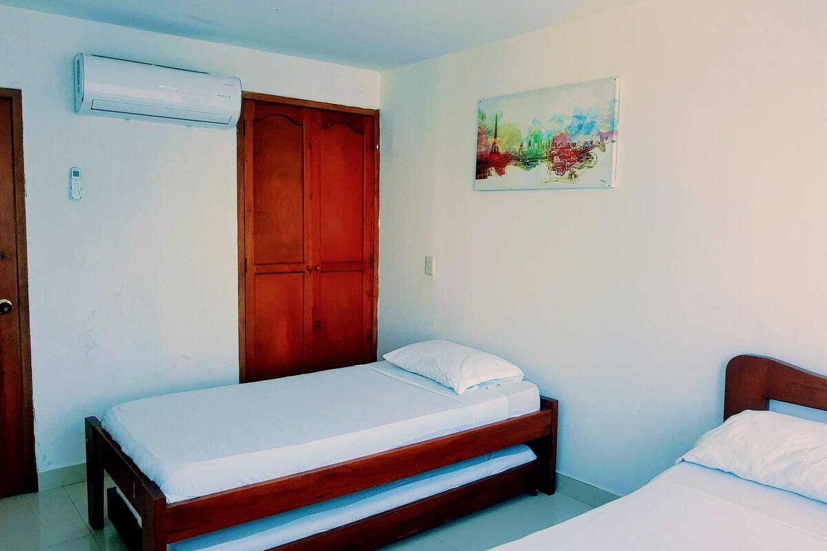 A bedroom with a wooden bed, a wardrobe, an air conditioner, and a painting on the wall.