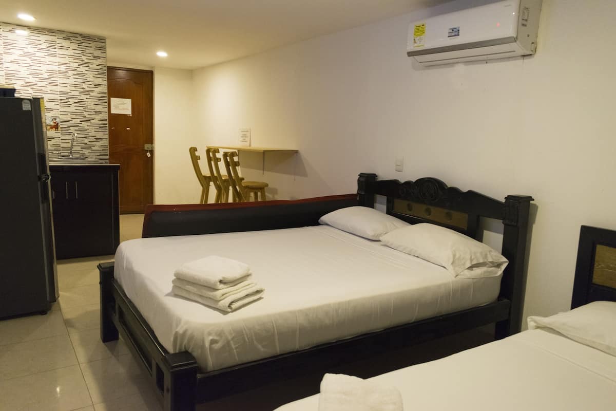 A hotel room with a large bed, a desk, a chair, a refrigerator, and a wall-mounted air conditioner.