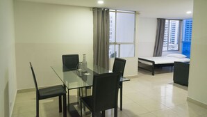 Een moderne hotelkamer met een glazen eettafel, vier stoelen, een bed en een groot raam met gordijnen.