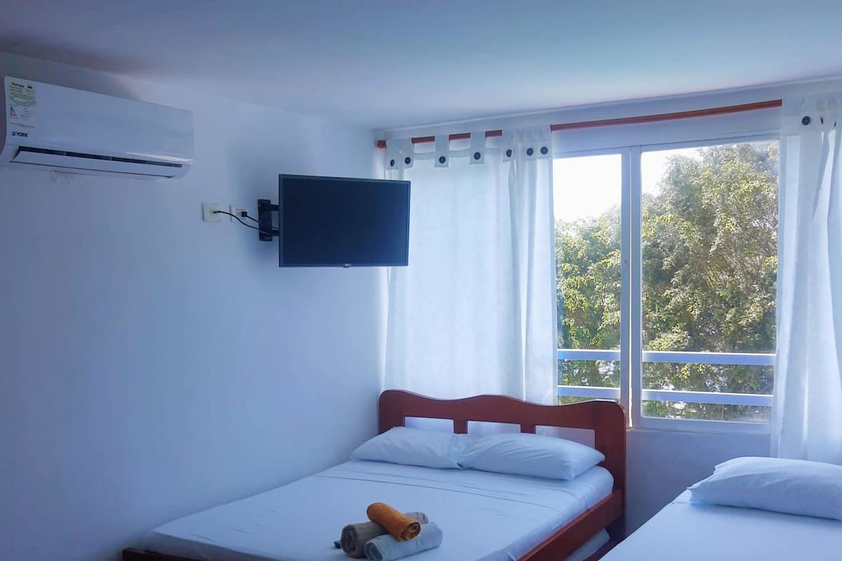 A bedroom with a bed, a TV mounted on the wall, and a window with curtains.