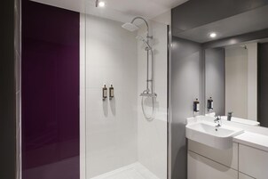 Een moderne badkamer met een douchecabine van glas, een witte wastafel en een grote spiegel.