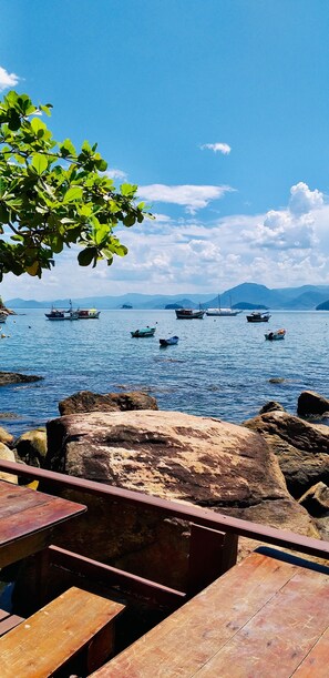 A wooden deck overlooking a calm lake with several boats, surrounded by rocks and a clear sky. - Pousada Sobre As Ondas De Picinguaba (Ubatuba)