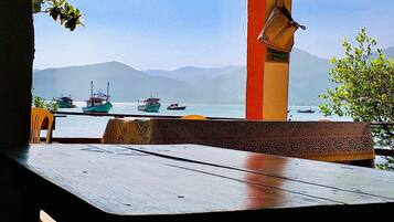 Une vue depuis un espace extérieur abrité, avec une table et des chaises, donnant sur une étendue d’eau où l’on aperçoit des bateaux et, au loin, des montagnes.